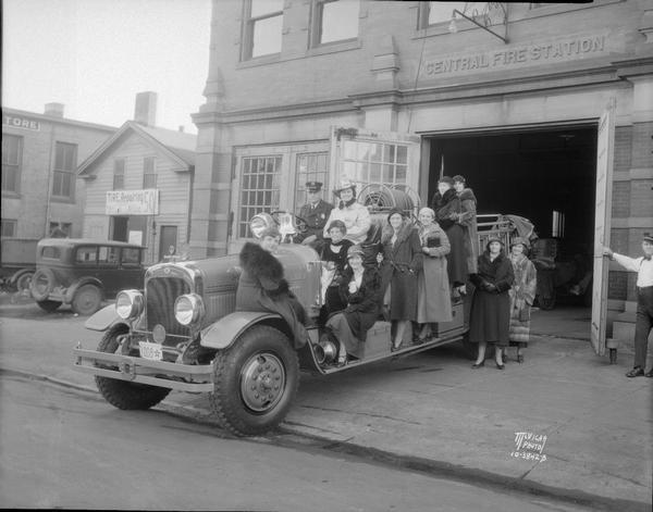 Group of Disabled American Veterans Auxiliary women on a fire truck parked in front of the Central Fire Station, 18-20 S. Webster Street. On the far left is Taylor's Tire Shop, at 22 S. Webster Street.