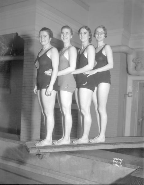 Four female Dolphin Club members posing in bathing suits on the diving board of the Lathrop Hall pool.