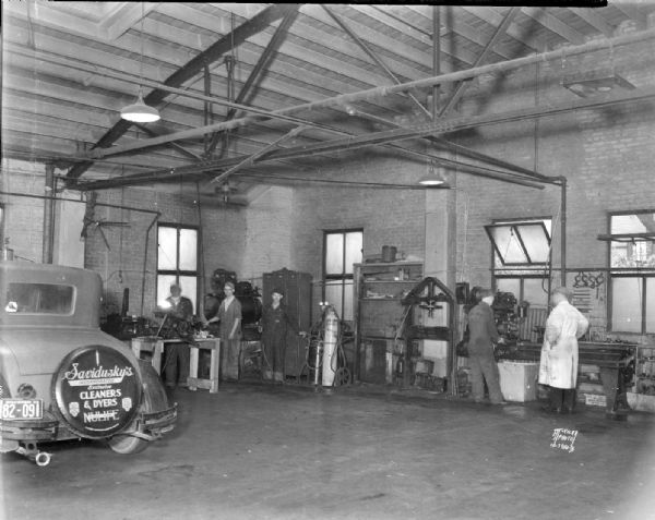 Interior of J.A. Brady garage and workshop, 1307-1309 Williamson Street.  Five men in photograph. The car on the left has Savidusky's Cleaners & Dyers advertising on the spare tire. Joseph A. "Doc" Brady died in 1931. John Eichman became manager.
