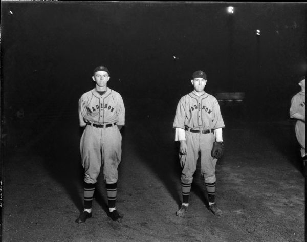 Outdoor portrait of two Madison Blues baseball players in uniform. Wilbur Freck has his hands behind his back, and Ray Gaffke is wearing a baseball glove.