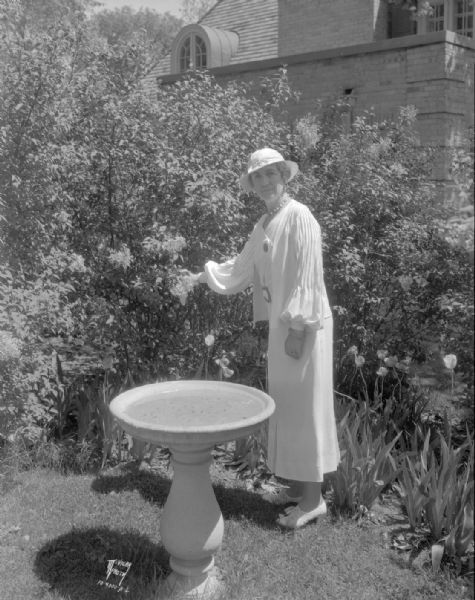 Jessie (Mrs. Harry) Manchester in her garden, with lilacs, tulips and a bird bath, in Maple Bluff.