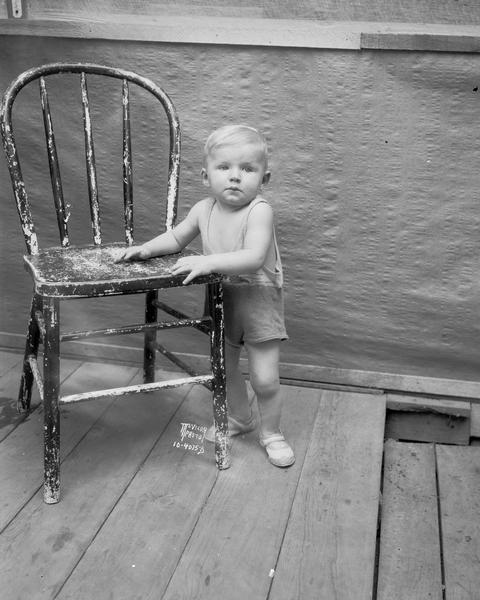Portrait of David Barr, son of University of Wisconsin Tent Colony Mayor Glenn Barr, at age 10 months, standing beside a chair. Family from Miami University, Oxford, Ohio. Also known as Camp Gallistella on the south shore of Lake Mendota, west of second point.