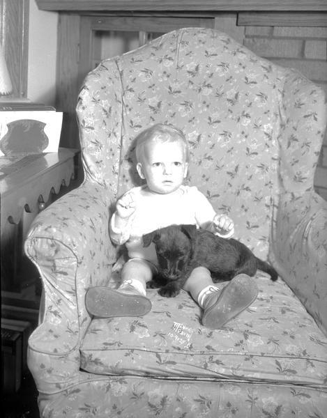 Jackie Taggart, 14-month-old son of Horace Taggart and Lenore Taggart, and their eight week old Scottie dog, Meg, sitting in a chair.