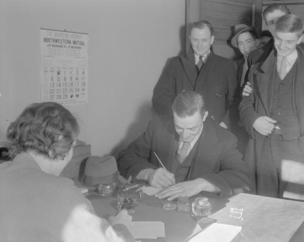 Doris Brobst, clerk for the Public Employment Office, sitting at her desk, 111 W. Main Street, registering a group of men for CWA (Civil Work Administration) employment.