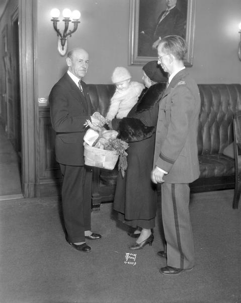 Governor Schmedeman presenting Christmas basket provided by the Volunteers of America to Mrs. Catherine Schwartz and daughter, Frances. Captain George Lawton, Volunteers of America, included.
