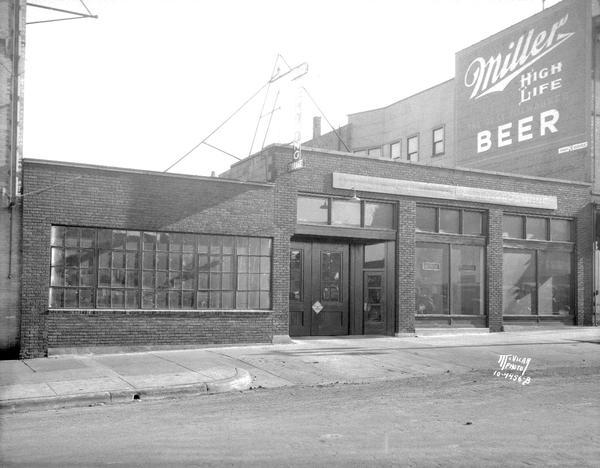 View across street towards the Dansin & Endres garage, 207 East Washington Avenue. Headed by "Danny" Dansin and Lee Endres. Shows "Miller High Life Beer" sign painted on the side of the building next door.