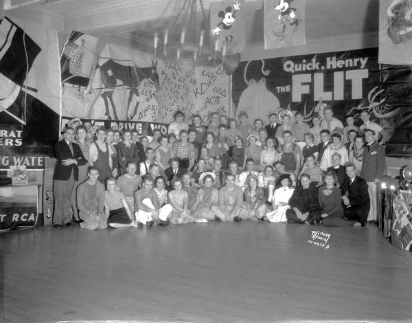 Group portrait of students in costume at the Acacia Fraternity, 108 Langdon Street, Bowery Party sign reads: "Quick, Henry, the Flit."