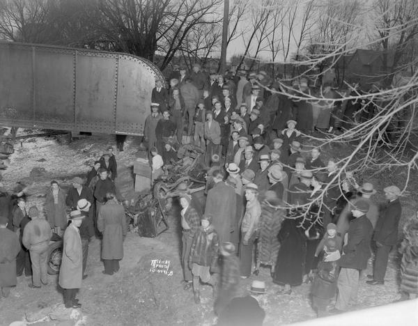 Crowd standing on the Thornton Avenue bank of the Yahara River at the Milwaukee Road railroad bridge looking at a car-train accident scene where Mrs. Clark Frothingham was killed.