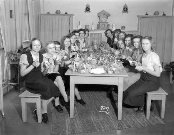 Fifteen YWCA Girl Reserves sitting around a table coloring Easter eggs and putting them in small baskets to be distributed to crippled children at the Wisconsin Orthopedic Hospital.