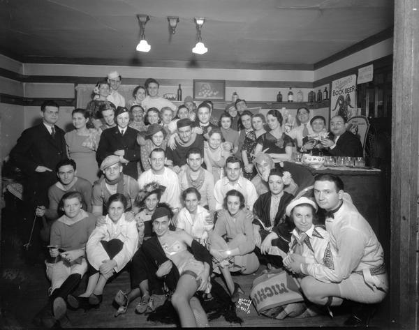 Group portrait of students in costume at Phi Delta Upsilon Bowery Party, 418 N. Frances. Shows Bock Beer poster on wall, and a sign that reads: "Drinks, One/Kiss."