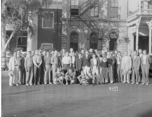 Group portrait of Soap Box Scooter champions and adults in front of the G.A.R. Hall, 118 Monona Avenue. Also shows portion of Monona Hotel, 114 Monona Avenue, and Elk's Club, 120-124 Monona Avenue. Soap Box event sponsored by Lincoln National Life Insurance.