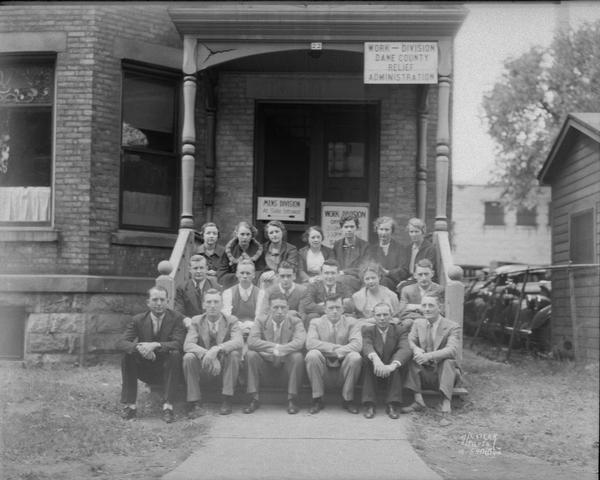 Group of men and women sitting on the steps in front of the Work Division Office, Dane County Outdoor Relief Administration, 22 W. Doty Street.