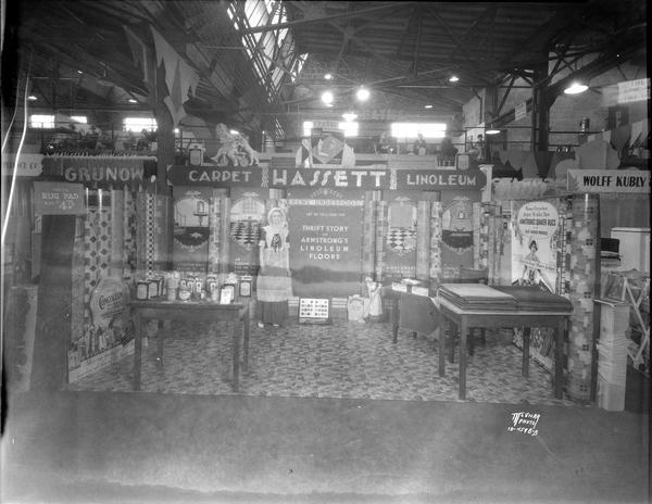 Woman, in costume, standing in Hassett Linoleum Co. display booth featuring Armstrong Products: carpet, linoleum, Armstrong Quaker rugs, at the Home Show.