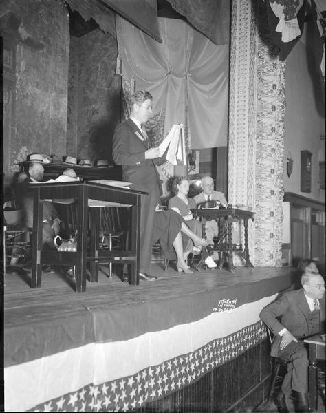 Former Governor Philip F. La Follette, the younger son of Robert M. La Follette, Sr., calling the roll on the proposal to form a new political party at the Progressive Party convention in Fond du Lac, Wisconsin. Several other people are sitting on stage. La Follette was elected to two more terms as the Progress Party candidate for governor.