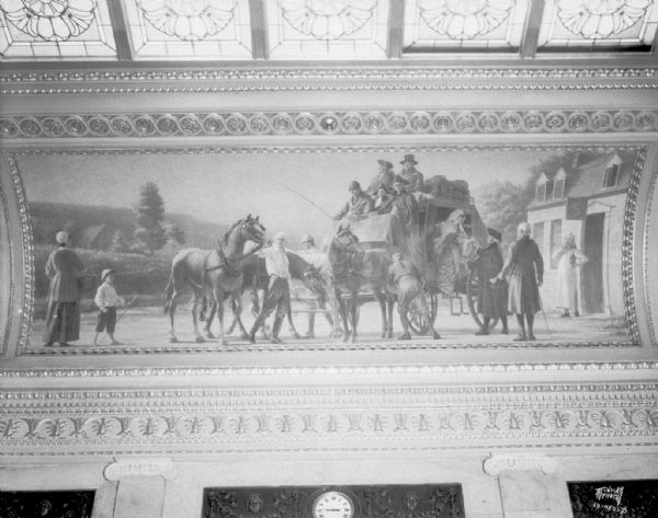 The mural depicts colonial period travel by stagecoach, which is halted at an inn while the horses are being changed. Some of the passengers are getting off. One of four murals by Charles Yardley Turner, representing the evolution of transportation in America. The stained glass skylight in the Wisconsin State Capitol North Hearing Room can also be seen. The title of the mural is: "The Stagecoach."