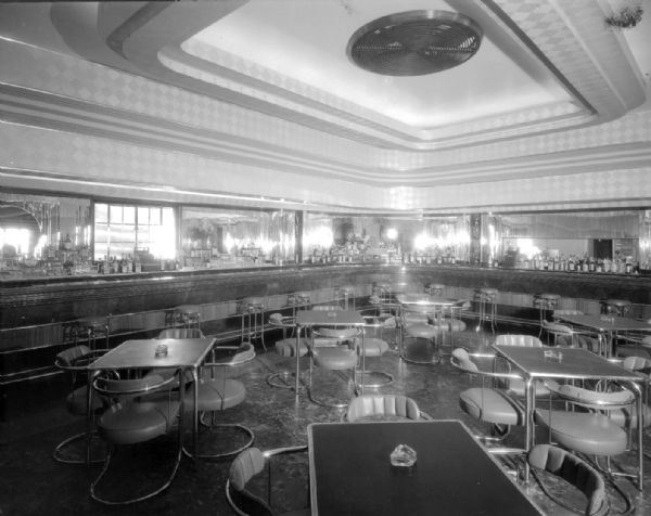 Interior of new Club Chanticleer Bar. The bar curves along the sides of the room, with tables and chairs in the foreground. Airport Road and Hwy. 12.