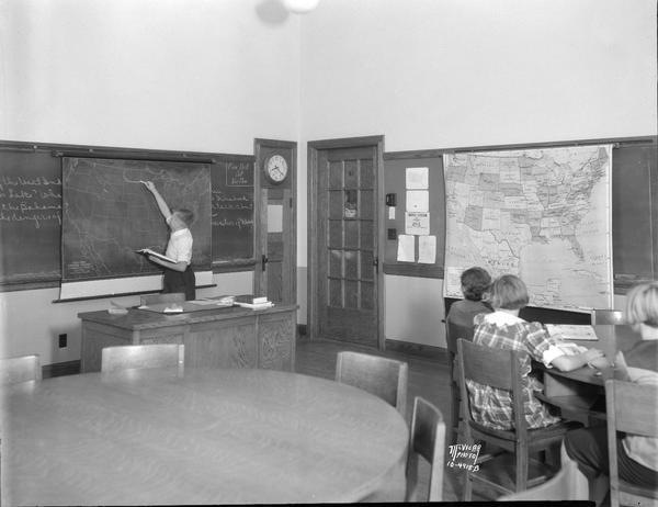 One West Junior High School student drawing on a U.S. map, with three other students looking on.
