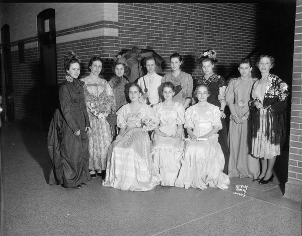 Eleven women, attending 80th reunion, wearing dresses that would have been worn by girls attending Central high school over the last 80 years.