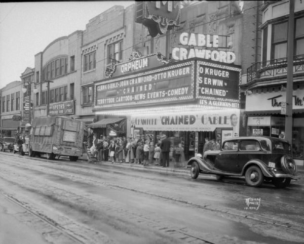 View down street towards a line of people waiting to view a rhinoceros enclosed in a truck parked in front of the Orpheum Theatre. The marquee reads: "Clark Gable - Joan Crawford - Otto Kruger in 'Chained.'"