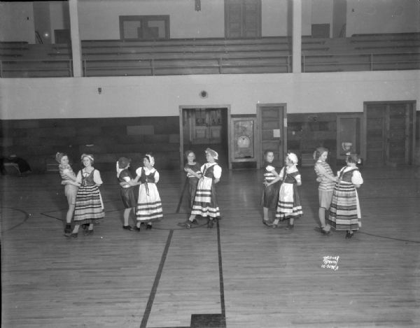 Nakoma School girls folk dance class, five "couples" dressed in ethnic costumes dancing with hands interlocked. Circle Dance.