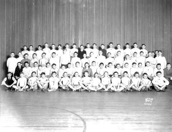 Group portrait of East High School boy's track team in uniform, and four coaches.