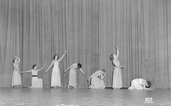 Seven girls performing a modern dance on stage.
