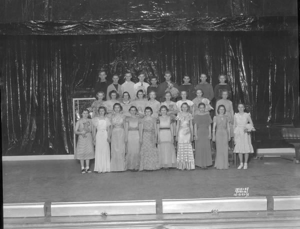 Group portrait of singers in costumes standing on risers on stage for the operetta "Tune In" presented by the East High A Capella Choir and Treble Clef Club.
