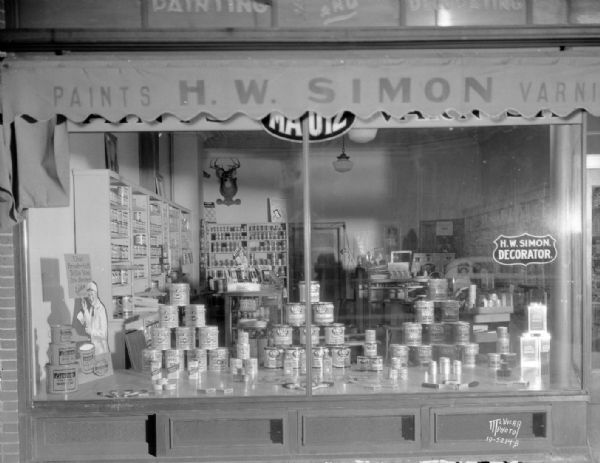 H.W. Simon Paint Store window, 1904 Monroe Street. Shows Mautz paint display and H.W. Simon, Decorator sign. The interior of the store can be seen through the window, and a deer trophy is hanging on the back wall.