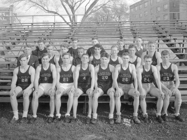 Group portrait of Central High School track squad in uniform sitting on bleachers.