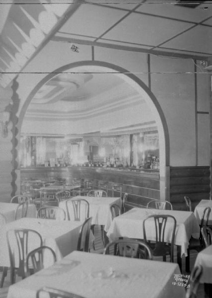 Club Chanticleer, looking at the barroom through an interior arch, with tables and chairs in the foreground.
