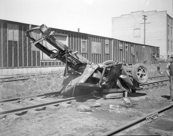 A Keystone Fuel & Material Co. truck after it was crushed by a Milwaukee Road train near the Brittingham Park crossing, Greenbush. Thomas Haney, truck driver, was seriously injured. A man is standing on the far right.