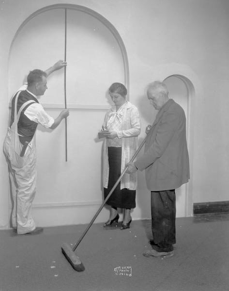 Workman measuring for window at Christ Presbyterian Church, 124 Wisconsin Avenue. A woman is taking notes and a man is sweeping.