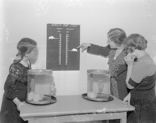 Teacher and two girls looking at rat growth chart.