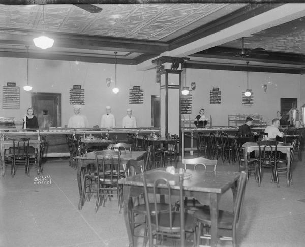 Interior view of Madison Cafeteria, 215 W. Washington Avenue. There are seven servers behind the counter, and two customers are sitting at tables.