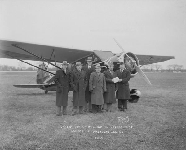 Six American Legion members with Stinson airplane, annual membership roundup, William B. Cairns Post, No. 57. Left to right: C.Y. Ballem, Ben Bull, Carl Christensen, John McGonigle, Arthur Wundrow, and Henry Robinson, pilot.