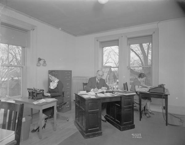 Three employees (one man, two women) of CUNA (Credit Union National Association) sitting at desks in their second floor office, 142 East Gilman Street. Shows old typewriter and adding machine.