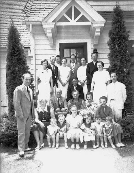 Group portrait of the Dieder family, with adults and children, posing on the front steps of a home.