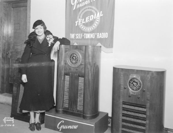 Woman, winner of radio contest, standing next to a Grunow floor model radio. Banner reads: "Grunow Teledial, the self-tuning radio" at the University Radio & Appliance Co., 702 State Street.