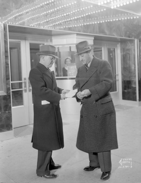 Flannery and Wohlenberg standing on the sidewalk in front of the Madison Theatre. A woman is inside the ticket booth.