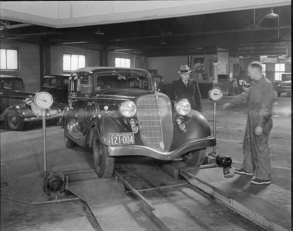 Close-up of two men testing front wheels of automobile at Eichman Garage, 1307-09 Williamson Street.
