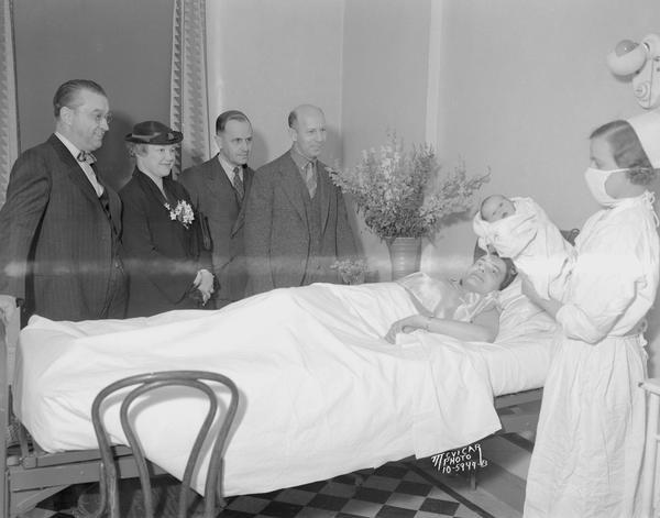 Evelyn Canfield, in Madison General Hospital bed, looks to her newborn baby, David, who won the Orpheum Theatre's fourth anniversary "A Star Is Born" contest. David is held by nurse Florence Louthain. Standing beside the bed from left to right are A.O. Paunack, Frances Ahlborn, E.A. Babcock and Phil Savidusky, representing companies who sponsored the contest.