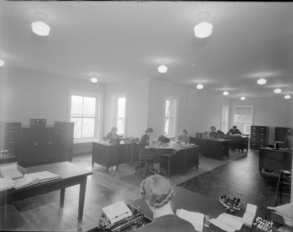 Remodeled C.U.N.A. (Credit Union National Association) office, Raiffeisen House 142 Gilman Street, after fire, taken from near the door, showing seven people working at their desks.