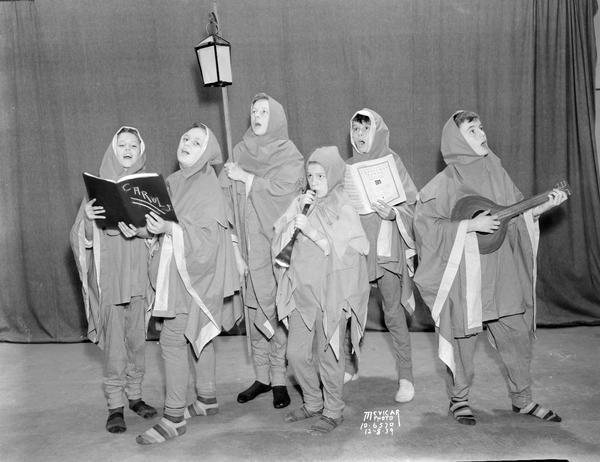 Group portrait of six East Side High School carolers posed in hooded garments, with musical instruments, 2218 East Washington Avenue.