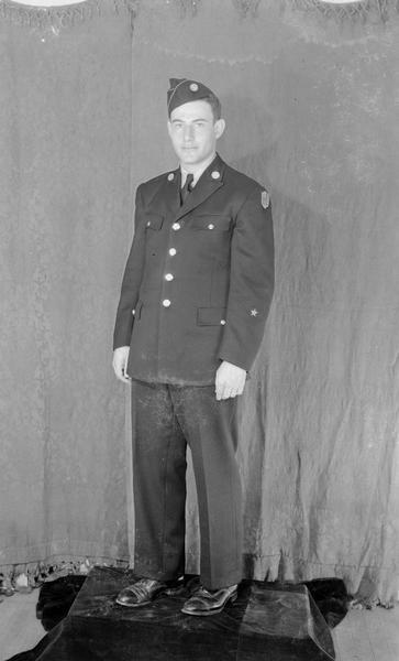 Full-length portrait of Herbert Bisno, of Tripp Hall, in his United States ROTC uniform. He is standing on a platform in front of a curtain.