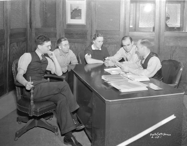 Five CUNA (Credit Union National Association) office workers seated around a desk at the new office, 1342 East Washington Avenue.