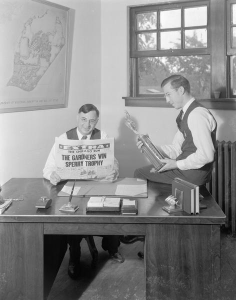 Louis Gardner seated with Chicago paper and Louis L. "Speed" Gardner holding Sperry trophy.