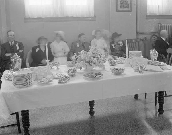 Two nurses and four elderly people sitting behind buffet table at St. Mary's Hospital, 720 South Brooks Street.