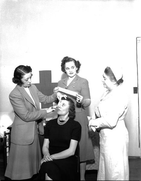 Two women applying bandages to a female patient with a nurse looking on. They are Wisconsin State Capitol employees learning first aid from the Red Cross.