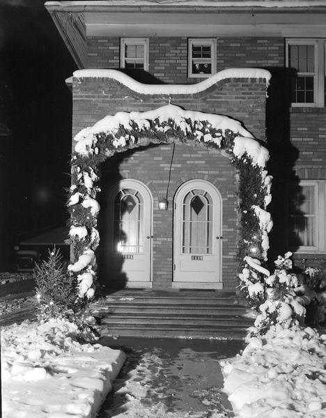 Christmas decorations over doorway of house with snow. James H. and Louise Behrend, 1126 Spaight Street; John P. and Elizabeth Behrend, 1128 Spaight Street.