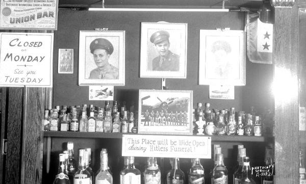Dobby's Cosmo Club, owned by John C. Dobson, Route 1, Mendota, Wisconsin, interior view of the bar showing liquor bottles and three World War II servicemen portraits (his sons ? Glenn, Jack, Robert and/or James) with AFL Union sign and sign saying: "This place will be wide open during Hitler's funeral!"